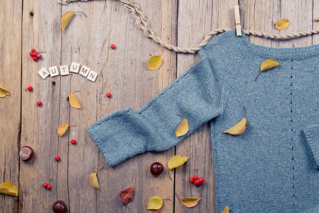 Autumn fall flat lay, top view. Warm knitted sweater, Fall Leaves, chestnuts, rowan berry and pumpkin with  inscription "autumn" on rustic wooden background