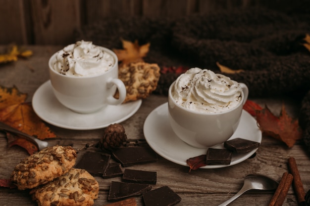 Autumn, fall leaves, hot steaming cup of coffee and a warm scarf on wooden table.