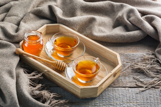 Autumn, fall, winter home decor in hygge style with drink. Seasonal composition with cup of hot tea with honey, warm woolen scarf, soft plaid on a rustic wooden table.