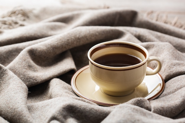 Autumn, fall, winter home decor in scandinavian, hygge style. Seasonal composition with cup of coffee, warm woolen scarf, soft plaid on a rustic wooden table.