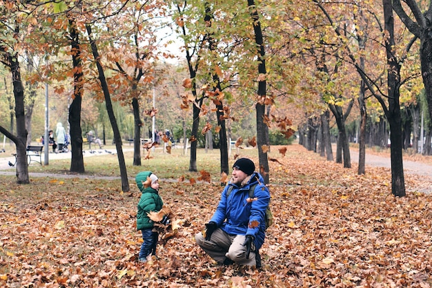 Осенняя семейная прогулка в лесу. Красивый парк с сухими желтыми листьями. Сын и отец, держась за руки.