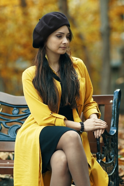 Autumn fashion. Gorgeous young woman sitting on the bench in street with yellow dress