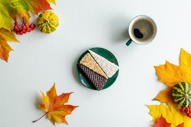 Lay piatto autunnale. su uno sfondo di legno bianco, dolci, cialde e una tazza di caffè tra foglie d'acero e zucche autunnali. foto orizzontale.