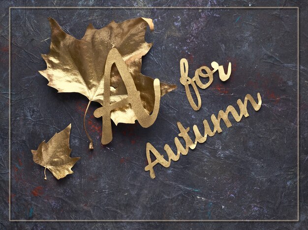 Autumn flat lay with painted golden leaves and text "A for Autumn" on dark textured bacgkrdound