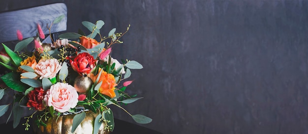 Autumn floral bouquet in punpkin vase on black chair, banner