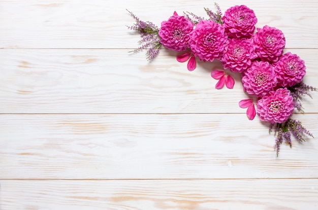 Motivo floreale autunnale con dalie rosa su fondo di legno bianco.