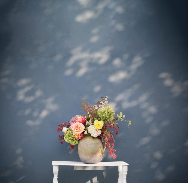 Autumn flowers and berries in rustic ceramic jug on background blue wall