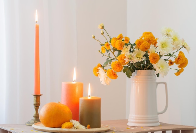 Autumn flowers with burning candles and pumpkins on vintage wooden shelf