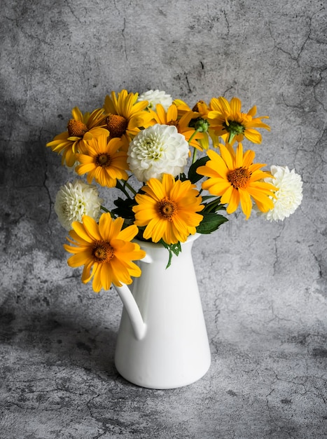 Autumn flowers yellow and white dahlias bouquet in a vintage white metal jug on a gray background