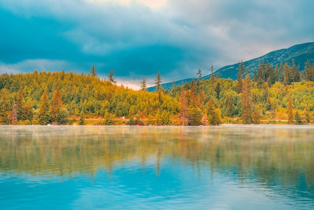 Autumn foggy sunrise landscape with tranquil peaceful mountain lake. Calmness nature in fall season