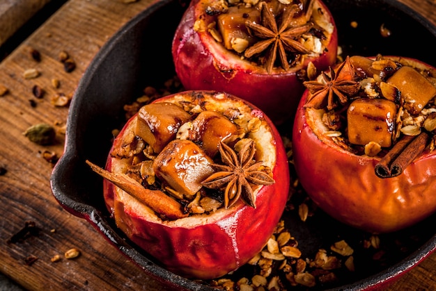 Autumn food recipes. Baked apples stuffed with granola, toffee and spices. On black stone table, in frying pan, copyspace