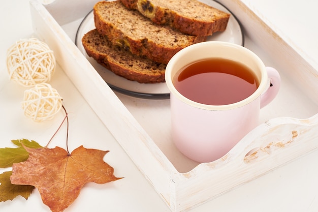 Autumn food-slices of banana bread, a Cup of tea, dry leaves, white wooden table. Cozy home winter