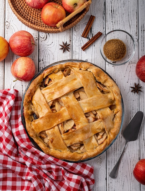 Autumn foods. Top view of homemade apple pie on white wooden table, decorated with apples, sugar and tablecloth