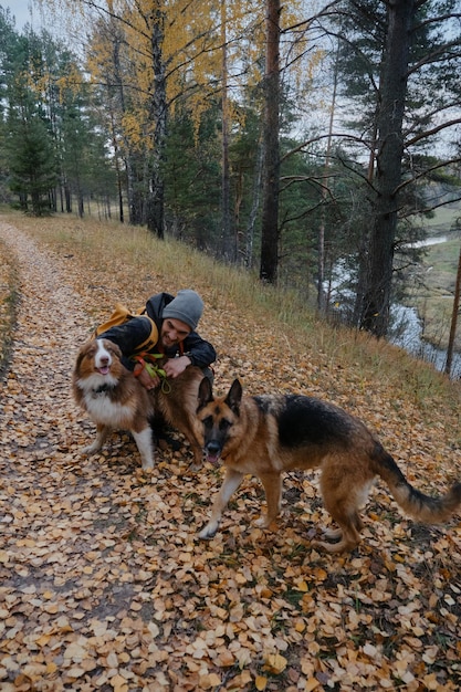가을 숲 절벽과 강은 백인 젊은이 아래로 흐릅니다. 가을 공원에서 두 마리의 개와 함께 산책