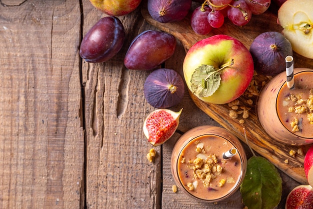 Autumn fruit smoothie yogurt drink Two glasses of whipped smoothie drink with fresh fall fruits berry plum figs apple oats and nuts wooden rustic background copy space