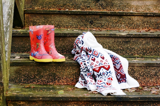 Autumn fruits on a vintage old wooden staircase. Autumn mood, warm clothes. Life style. Porch of the old house. Red  Rubber boots.