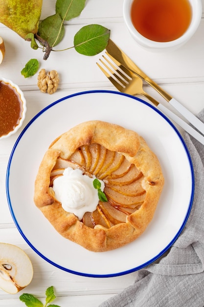 Foto galette d'autunno con gelato di pere, noci, salsa caramellata e cannella su uno sfondo bianco di legno