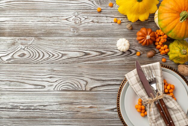 写真 秋の収穫コンセプト プレート ナイフ フォーク ナプキン生野菜カボチャ パティパン クルミ ナナカマドの果実とドングリの平面図写真 copyspace と分離の灰色の木製机の背景に