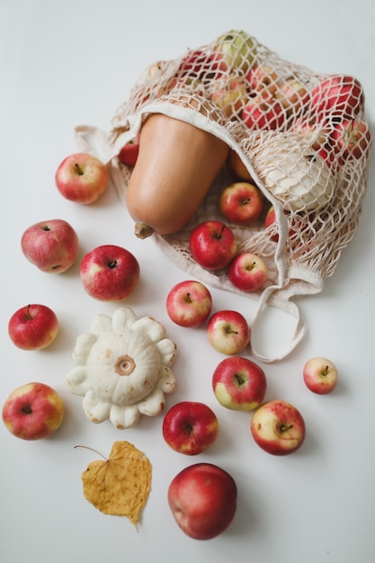 Autumn harvest with sqush pumpkin red apples in a mesh shopping eco bag on a white background