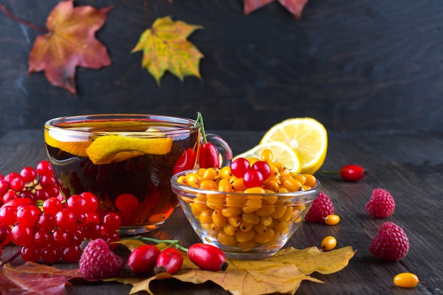Фото Осень здоровые напитки концепция. чашка чая с осенними ягодами облепихи, калины, шиповника, рябины и осенних листьев. пить с витамином с