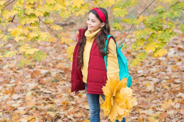 秋の子供のファッション。インスピレーションのためのロマンチックな季節。幸せな子供時代。学校に戻る。バックパックを持つ10代の少女は、公園でカエデの葉を保持します。秋の季節の美しさ。森の中で一日をお楽しみください。フォローしてください。