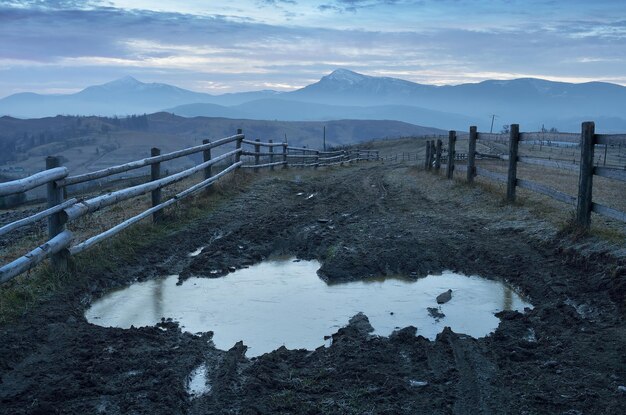 Autumn landscape frosty morning. Road with frozen puddle and swamp. Wooden fence in a mountain village. Carpathians, Ukraine, Europe