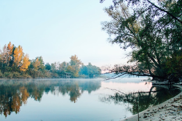 Autumn landscape over the river. Fog. Reflection of yellow trees in the water