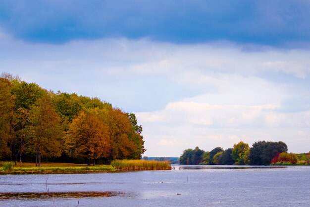 Autumn landscape with river and forest on river bank in cloudy weather