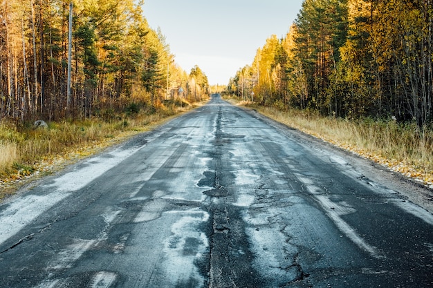 Autumn landscape with road by damaged asphalt, trees and sky