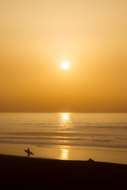 サーファーのシルエットでビーチに沈む夕日の暖かい色と秋の風景