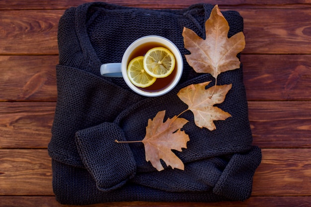 Autumn layout with hot tea with a lemon on a sweater and dry leaves.