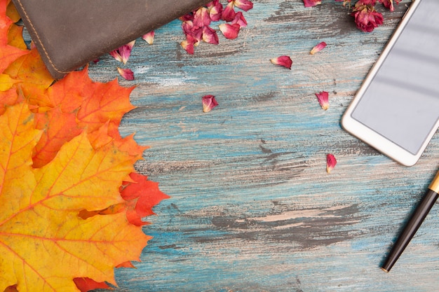 Autumn layout with yellow-orange leaves, pen and notebook, dry rose petals. copy space