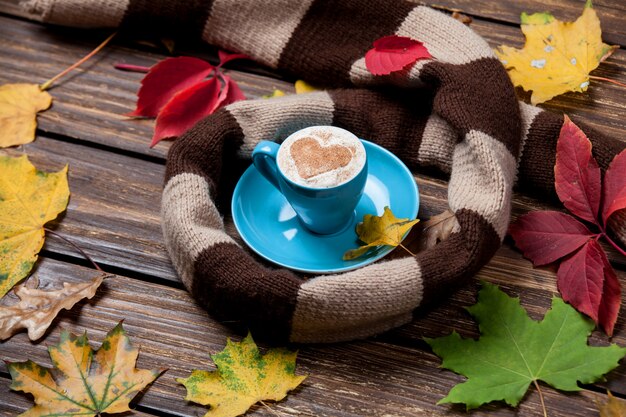 Autumn leafs, scarf and coffee cup on wooden table.