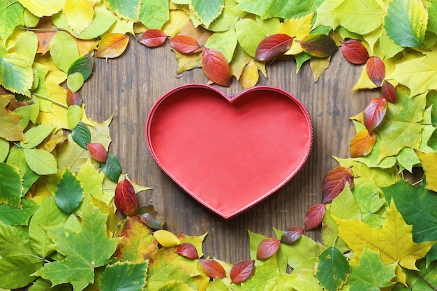 Autumn leaves background in shape of heart on wooden table