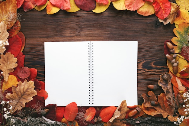 Autumn leaves and paper notebook on wood