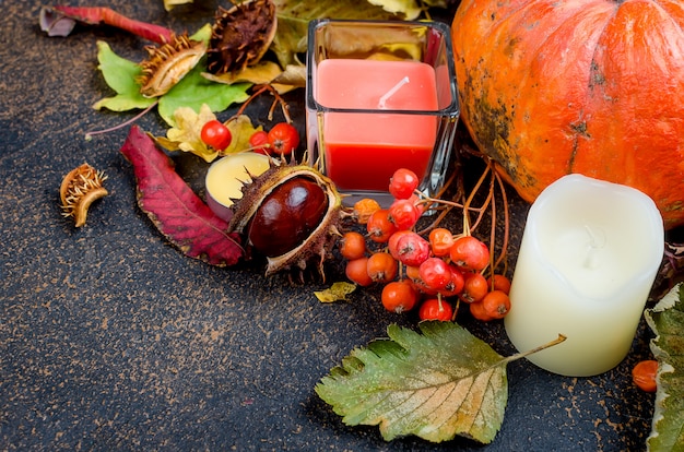 Autumn leaves, pumpkin, chestnuts, candles on a dark background