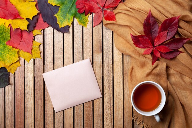 Autumn leaves, white tea cup on table, textile napkin, wooden background