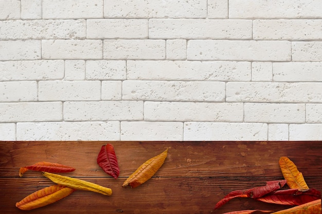 Autumn leaves on wooden table against white brick wall with space for text or object, banner design