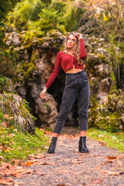 Autumn lifestyle blonde Caucasian girl in a red sweater enjoying nature in a park Enjoying nature with a natural cave