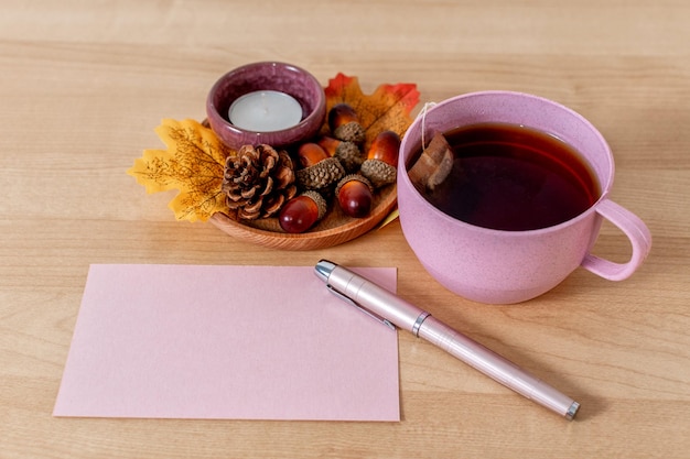 Autumn mood composition on a wooden table with tea cup greeting card and leaves