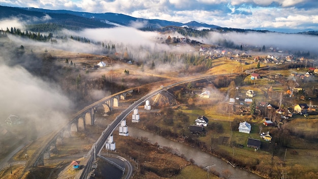 Autumn morning, foggy mountain valley. Railroad bridge, old Vorohta viaduct. Village on hills covered by clouds. Fall rural landscape. Misty cold November morning. Carpathian range, Ukraine, Europe.