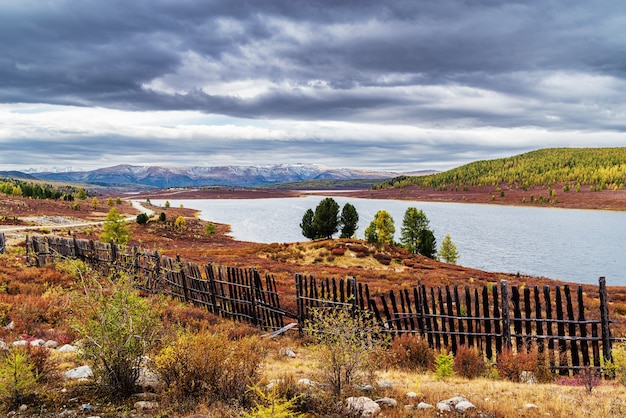 Autumn mountain landscape old wooden fence on shore of Uzunkel lake Altai Russia