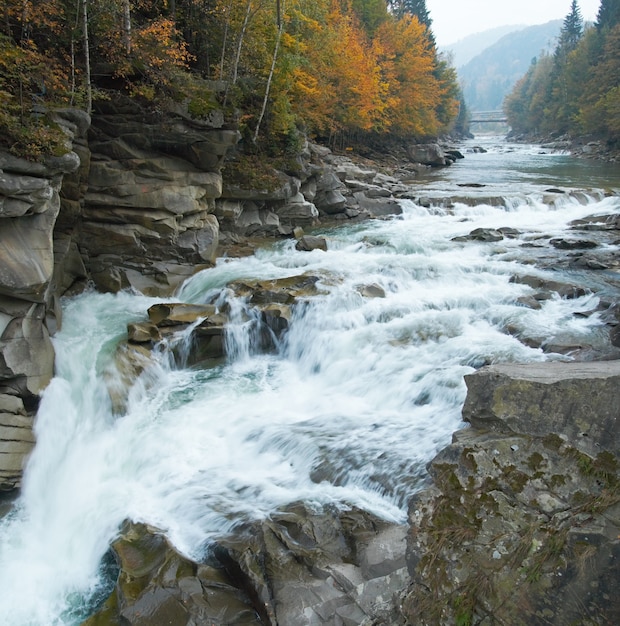 Autumn mountain river viev with waterfall and bridge