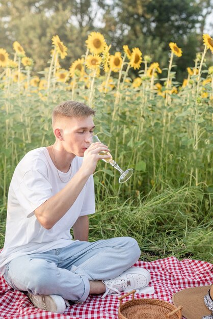 秋の自然。楽しさと嘘つき。シャンパンを飲んで日没のひまわり畑でピクニックをしている10代の少年