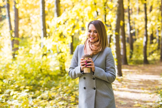 秋、自然、人々の概念-の背景に公園に立っている青いコートの若い女性