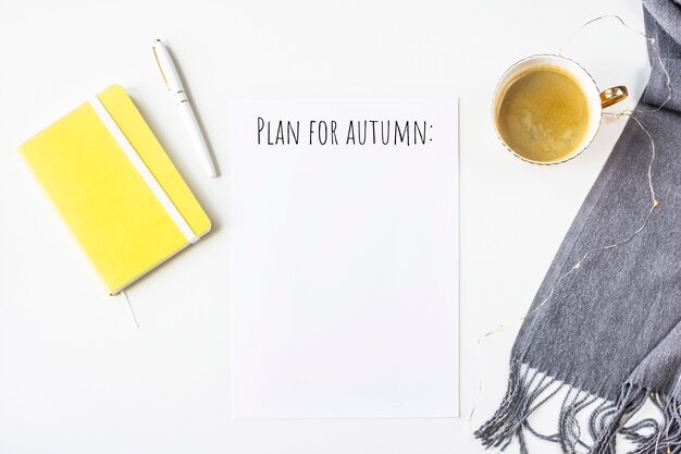 Autumn notes on a white table next to a scarf, yellow notepad 