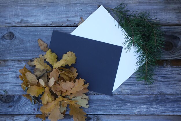 Composizione autunnale di foglie di quercia e rami di pino con fogli di carta vuoti su fondo di legno invecchiato