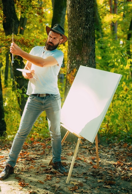 Photo autumn outdoor portrait of artist he painting autumn picture man artist painting autumn picture