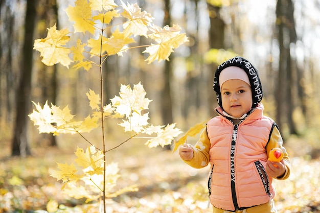 Autumn outdoor portrait of beautiful happy baby girl in forest with woodpecker toy in hands against yellow leaves