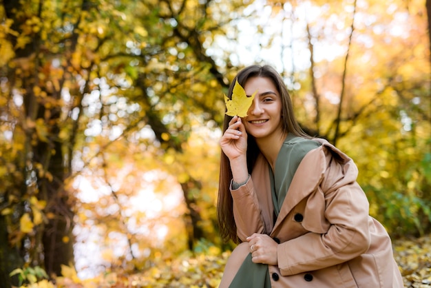 Autumn park. Beautiful woman in green dress posing in autumn park with yellow leaves